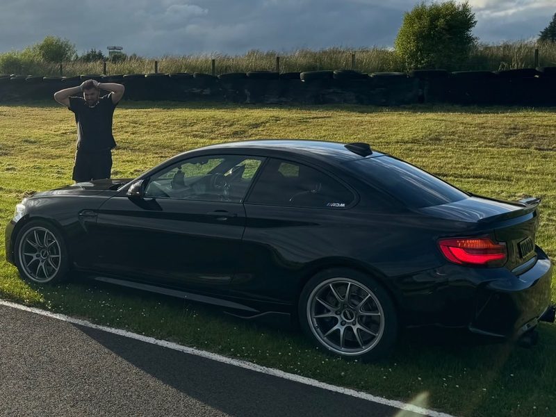 Robbie's black F87 M2 parked on the grass at a circuit